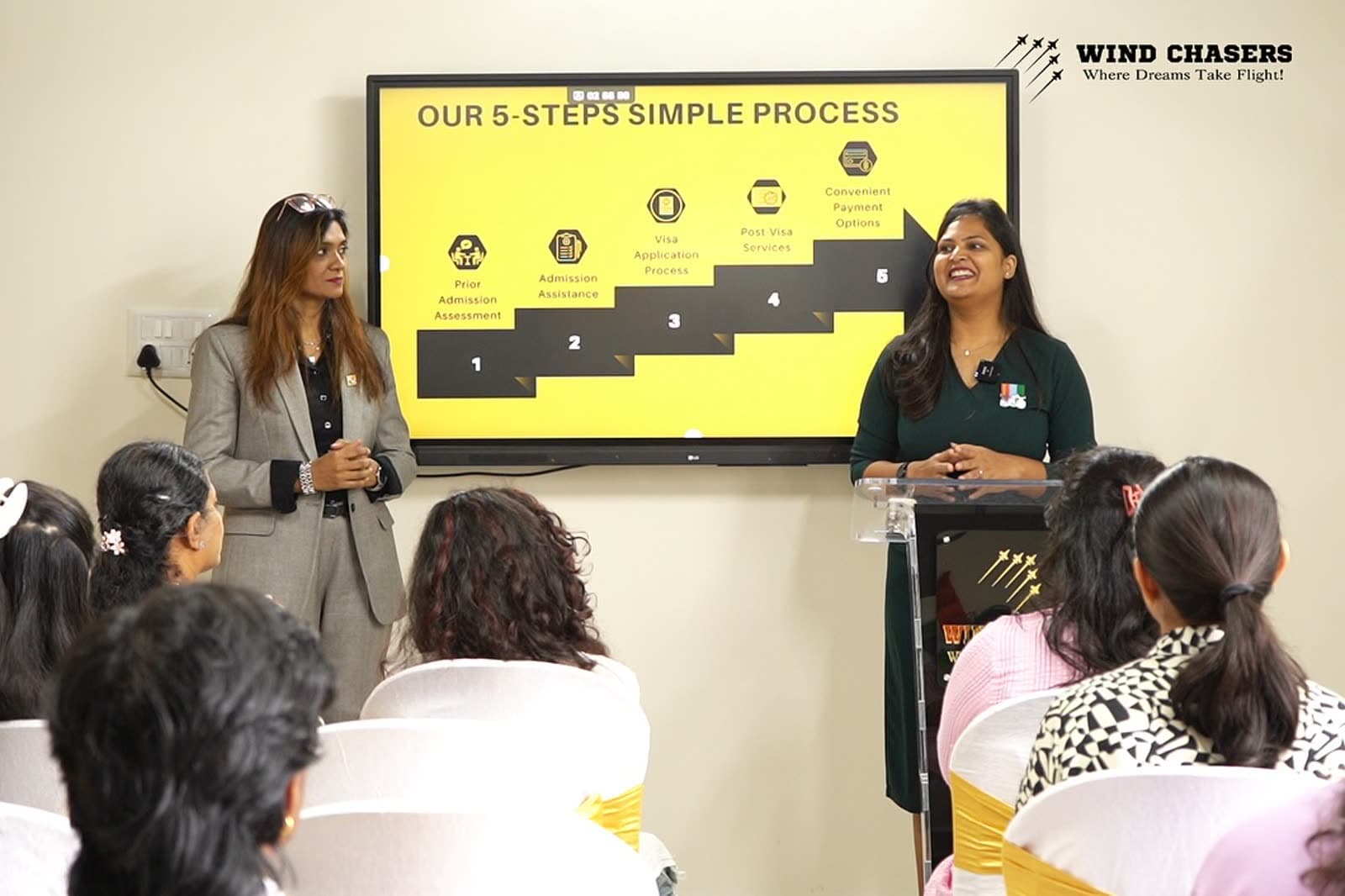 Two women presenting the WindChasers admissions process to a seated audience