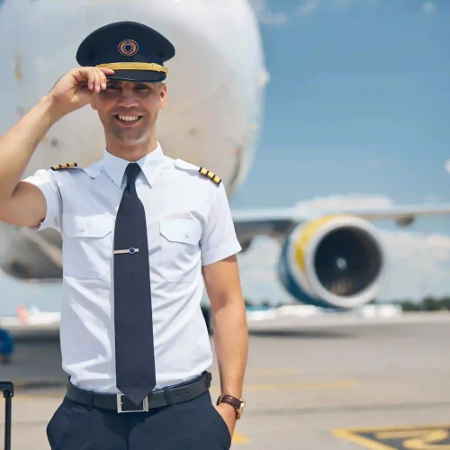 cheerful-young-man-airline-worker-touching-captain-hat-smiling-while-standing-airfield-with-airplane-background